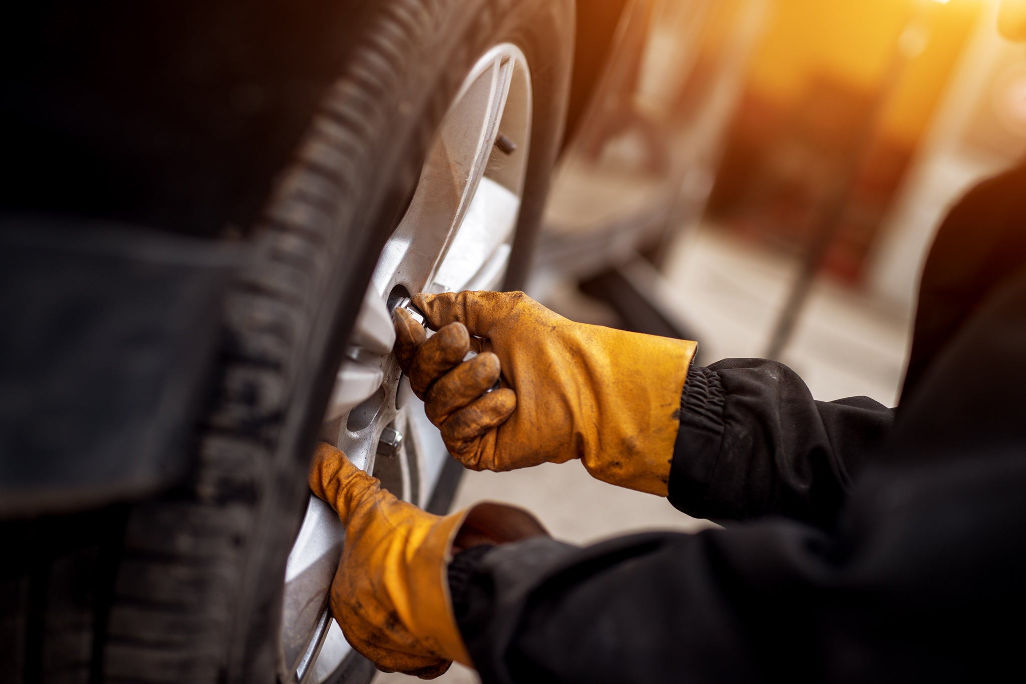 An experienced mechanic with orange gloves is putting screws on a placed wheel on a car.