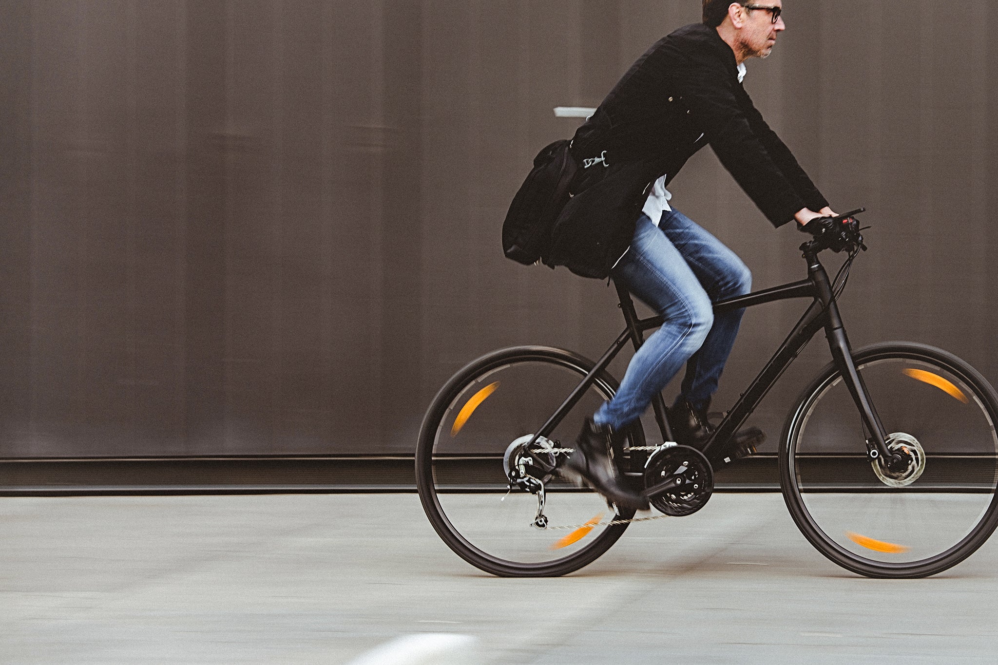 Sustainability Handsome man, on the way to work, riding bicycle beside the grey wall. The man is casually dressed and wears eyeglasses and carries black briefcase hung on shoulder. Blurred motion, copy space has been left.