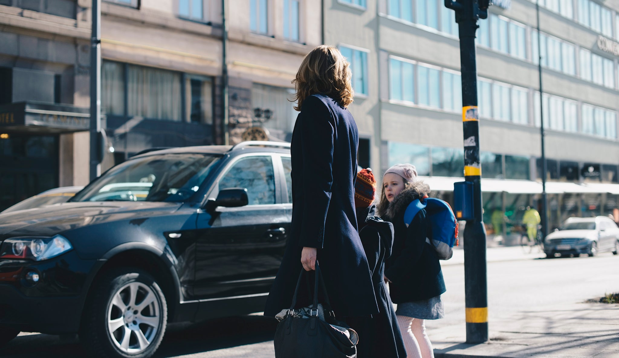 A woman with two children are crossing the street.