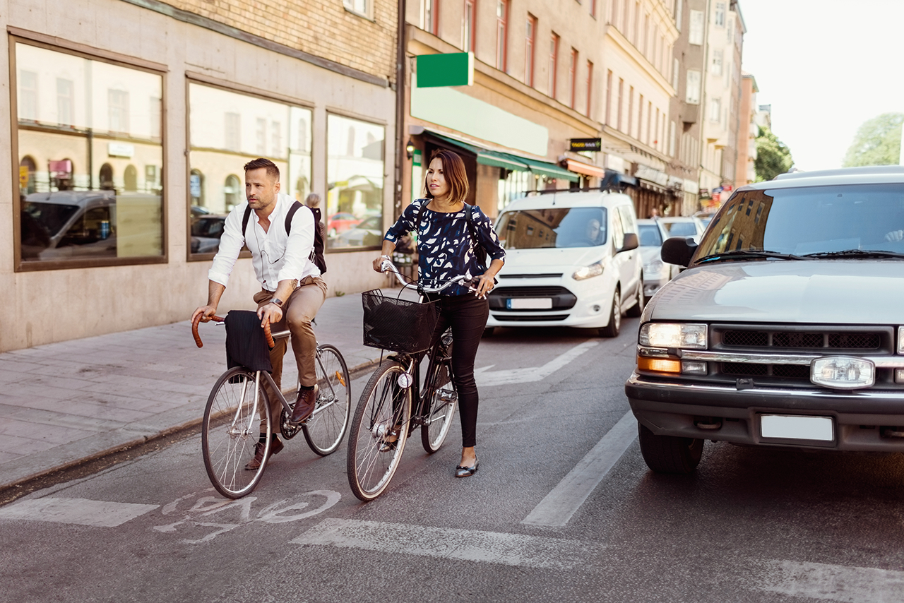 A man and a woman on their bicycles next to a car waiting for the traffic lights.