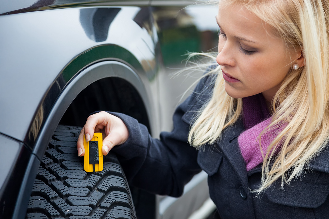 A young woman is measuring the tread depth of her car tire.